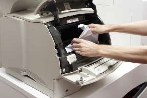 A man's hands freeing up a paper jam in an opened office printer